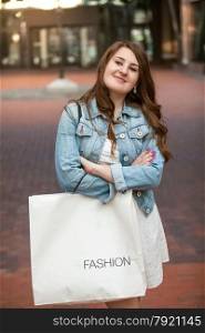 Beautiful smiling woman with white paper shopping bag on street
