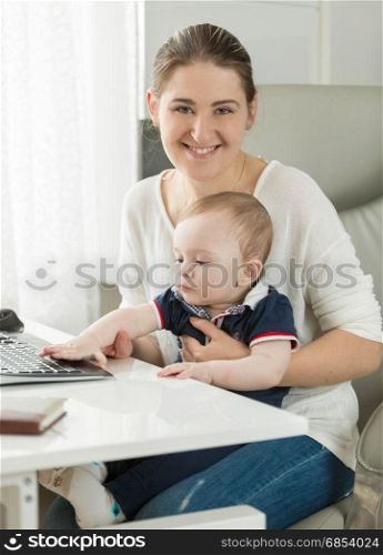 Beautiful smiling woman working on computer with her baby son