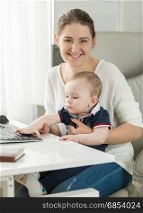 Beautiful smiling woman working on computer with her baby son