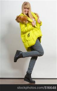 Beautiful smiling young fashionable girl wearing jacket with hood posing raising leg. Preparing herself clothes. Fashion in winter time.. Fashion girl in jacket.