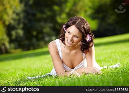 Beautiful smiling young woman lies on a lawn in a summer garden