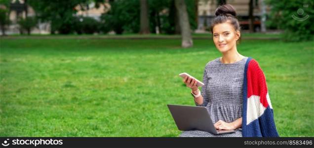 Beautiful smiling young woman sitting on the bench with smartphone and laptop in the park. Woman with smartphone and laptop