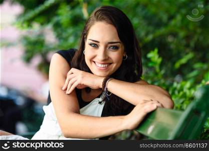 Beautiful smiling young woman with blue eyes looking at camera sitting on urban bench. Happy girl in casual clothes. Lifestyle concept.