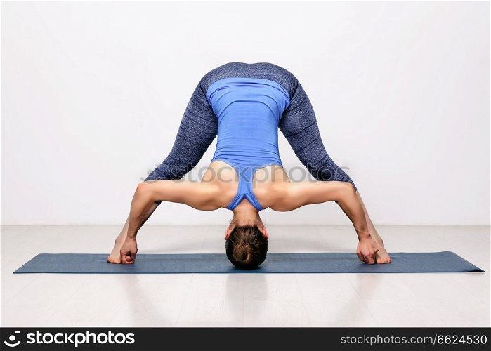 Beautiful sporty fit woman practices Ashtanga Vinyasa yoga asana Prasarita padottanasana D - wide legged forward bend D. Sporty woman practices Ashtanga Vinyasa yoga asana