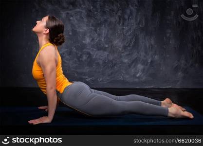 Beautiful sporty fit yogini woman practices yoga asana urdhva mukha svanasana - upward facing dog pose on dark background. Sporty fit yogini woman practices yoga asana Urdhva mukha svanas