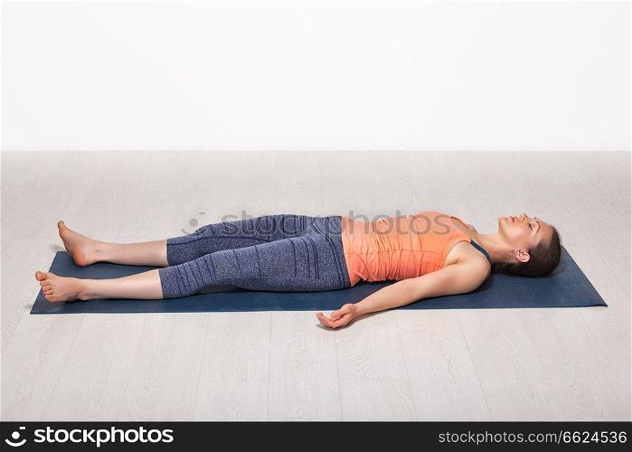 Beautiful sporty fit yogini woman relaxes in yoga asana Savasana - corpse pose in studio. Sporty fit girl relaxes in yoga asana Savasana