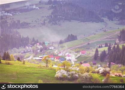 Beautiful spring landscape. Blooming garden flower trees. Traditional mountain village on hills. Orchard blossom. Rural Ukraine Carpathian sunrise. Smoke clouds.