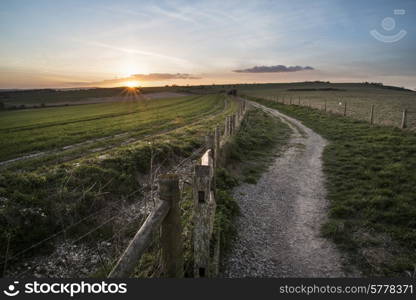 Beautiful Spring landscape of gate leading into fields with setting sun on horizon