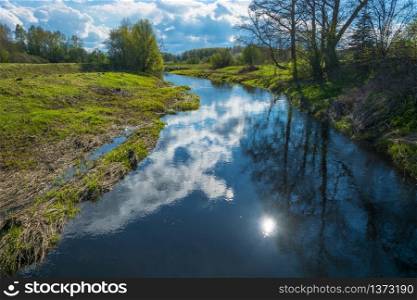 Beautiful spring landscape with reflection of sun and clouds in the water of a small river.