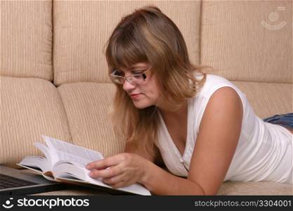 Beautiful student girl lying on the sofa with book and laptop.