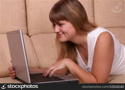 Beautiful student girl lying on the sofa with laptop.