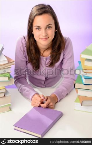 Beautiful student girl sitting between stacks of books purple background