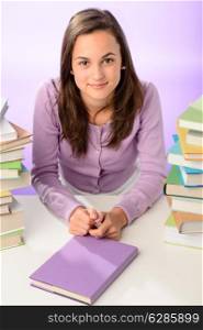 Beautiful student girl sitting between stacks of books purple background