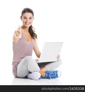 Beautiful student sitting in the floor with a laptop and thumbs up, isolated in white