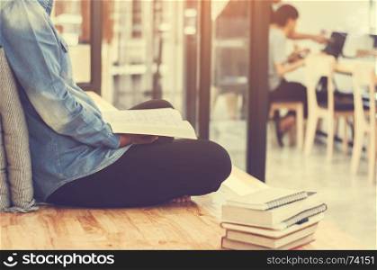Beautiful student woman sitting at the stair and reading a book with blurred cafe workplace
