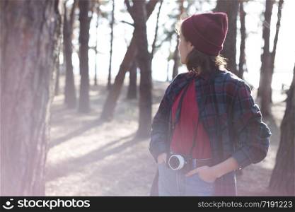 beautiful stylish girl holding a camera in the forest at sunset time