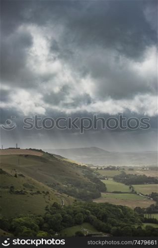 Beautiful Summer landscape image of escarpment with dramatic storm clouds and sun beams streaming down