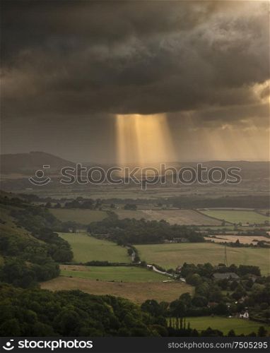 Beautiful Summer landscape image of escarpment with dramatic storm clouds and sun beams streaming down