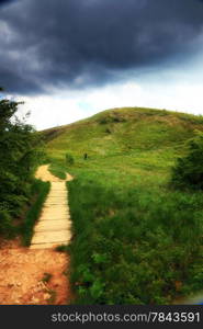 Beautiful summer landscape in the mountains. Pathway through the grassy hills, dark sky with clouds Bieszczady Poland