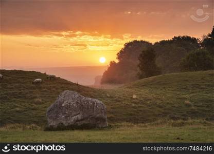 Beautiful Summer sunrise landscape of Neolithic standing stones in English countryside with gorgeous light with background mist