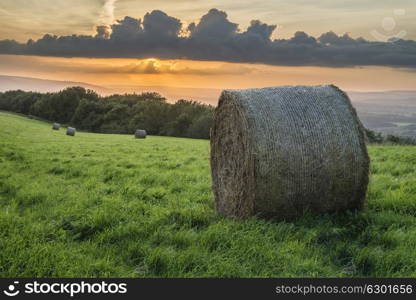 Beautiful Summer sunset over countryside landscape of field with hay bales