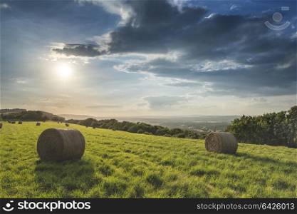 Beautiful Summer sunset over countryside landscape of field with hay bales