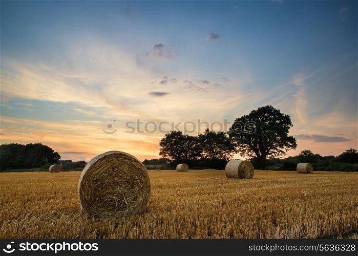 Beautiful Summer sunset over field of hay bales in countryside landscape