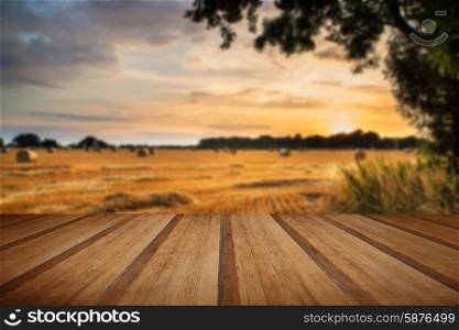 Beautiful Summer sunset over field of hay bales in countryside landscape with wooden planks floor