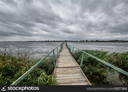 Beautiful summer view on beautiful lake, long wooden bridge and dramatic sky. Serene lake and a bridge without people. Landscape. Destination concept.