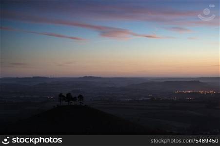 Beautiful sunrise dawn landscape of countryside overlooking brightly lit town in valley below