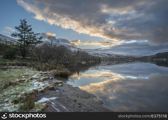 Beautiful sunrise landscape image in Winter of Llyn Cwellyn in Snowdonia National Park with snow capped mountains in background