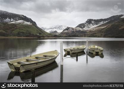 Beautiful sunrise landscape image in Winter of Llyn Nantlle in Snowdonia National Park with snow capped mountains in background