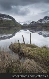 Beautiful sunrise landscape image in Winter of Llyn Nantlle in Snowdonia National Park with snow capped mountains in background