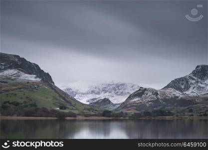 Beautiful sunrise landscape image in Winter of Llyn Nantlle in Snowdonia National Park with snow capped mountains in background