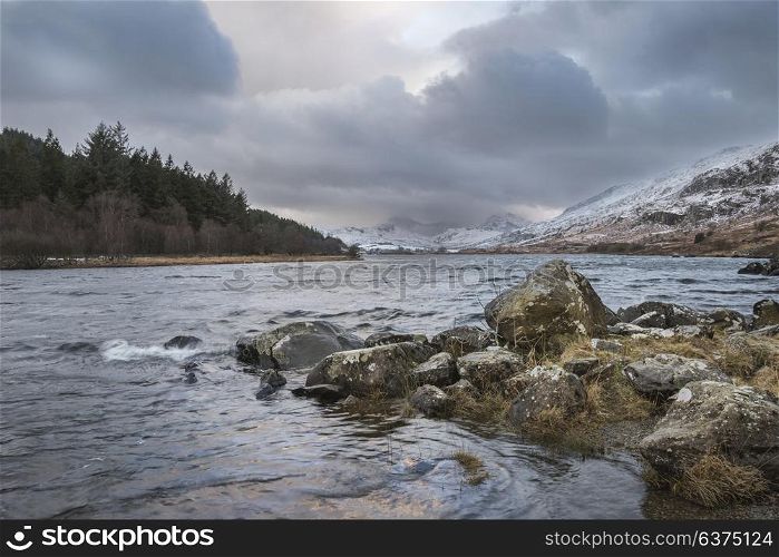 Beautiful sunrise landscape image in Winter of Llynnau Mymbyr in Snowdonia National Park with snow capped mountains in background