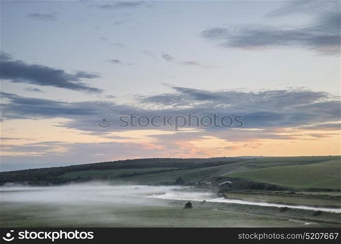 Beautiful sunrise landscape over English countryside with river slowly flowing through fields