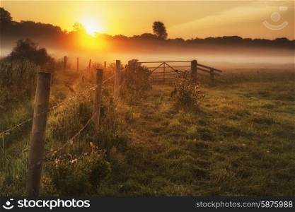 Beautiful sunrise landscape over foggy English countryside with glowing sun