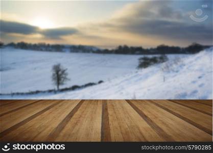 Beautiful sunrise landscape over snow covered Winter countryside with wooden planks floor
