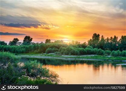 Beautiful sunset above a big river with green forest on the other coast and reflection on water