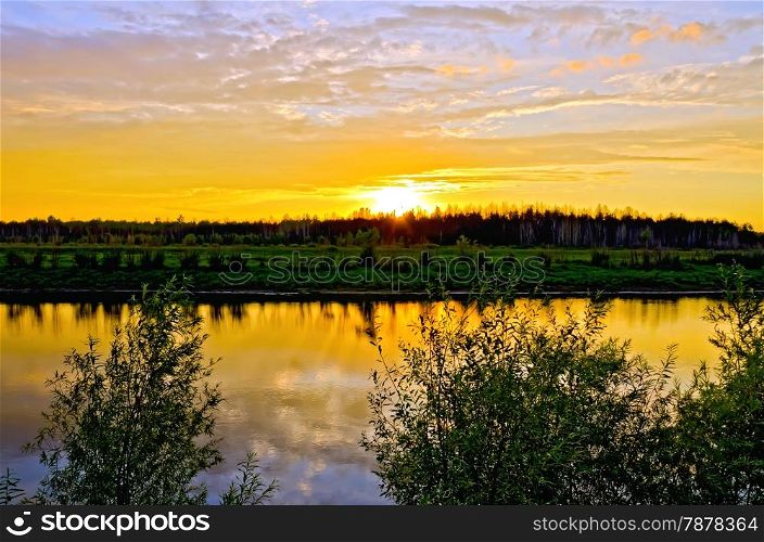Beautiful sunset, clouds, painted in red and orange colors, forest, coast and their reflection in the river