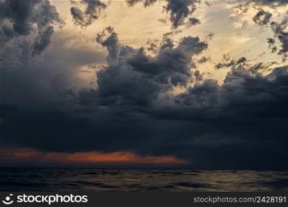 Beautiful sunset cloudy pre-stormy sky and dark sea water, evening seascape. Horizontal color photograph.