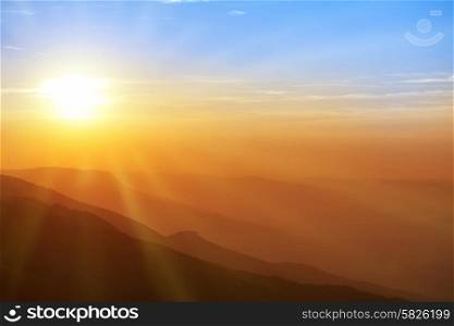 Beautiful sunset in the mountains. Colorful landscape with sun, sunrays and blue sky