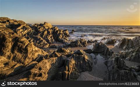 Beautiful sunset landscape image of calm sea against rocky shoreline