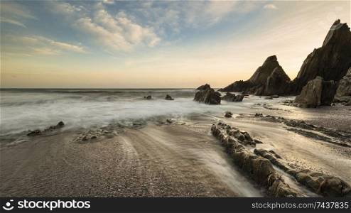 Beautiful sunset landscape image of Westcombe Beach in Devon England with jagged rocks on beach and stunning cloud formations