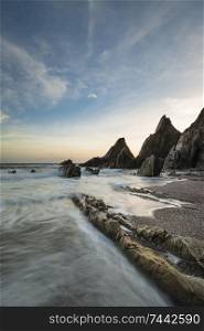 Beautiful sunset landscape image of Westcombe Beach in Devon England with jagged rocks on beach and stunning cloud formations