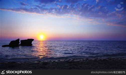 Beautiful sunset on the beach, seascape with calm ocean and rocks in the blue water