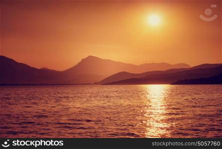 Beautiful sunset on the sea, majestic peaceful seascape, great mountains silhouette in orange sun light, beauty of nature concept