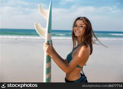 Beautiful surfer girl at the beach holding a surfboard and smiling