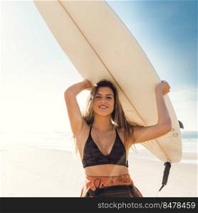 Beautiful surfer girl holding a surfboard over her head and smiling