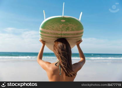 Beautiful surfer girl holding a surfboard over her head while looking to the waves